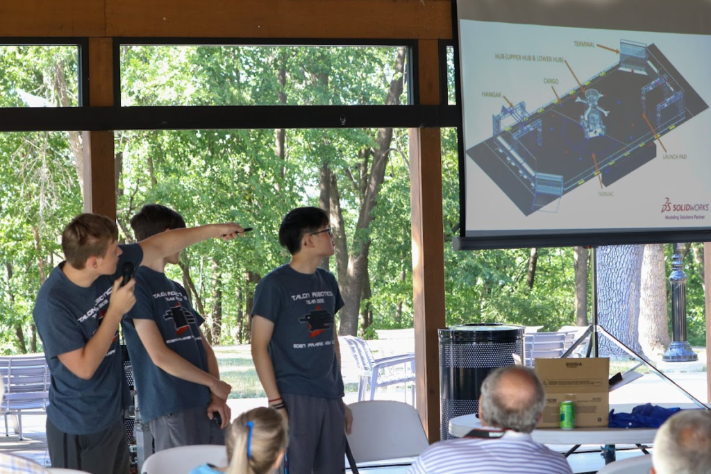 Three students using a lazer pointer to present infront of a crown of people.