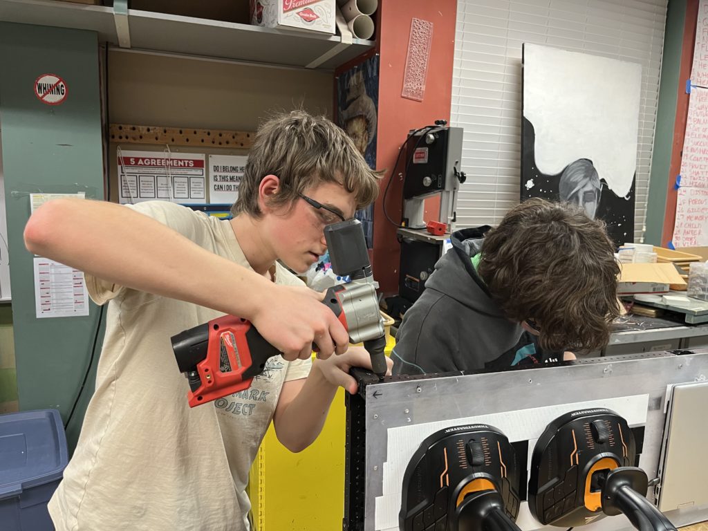 Two team members using a rivet gun on a metal surface.