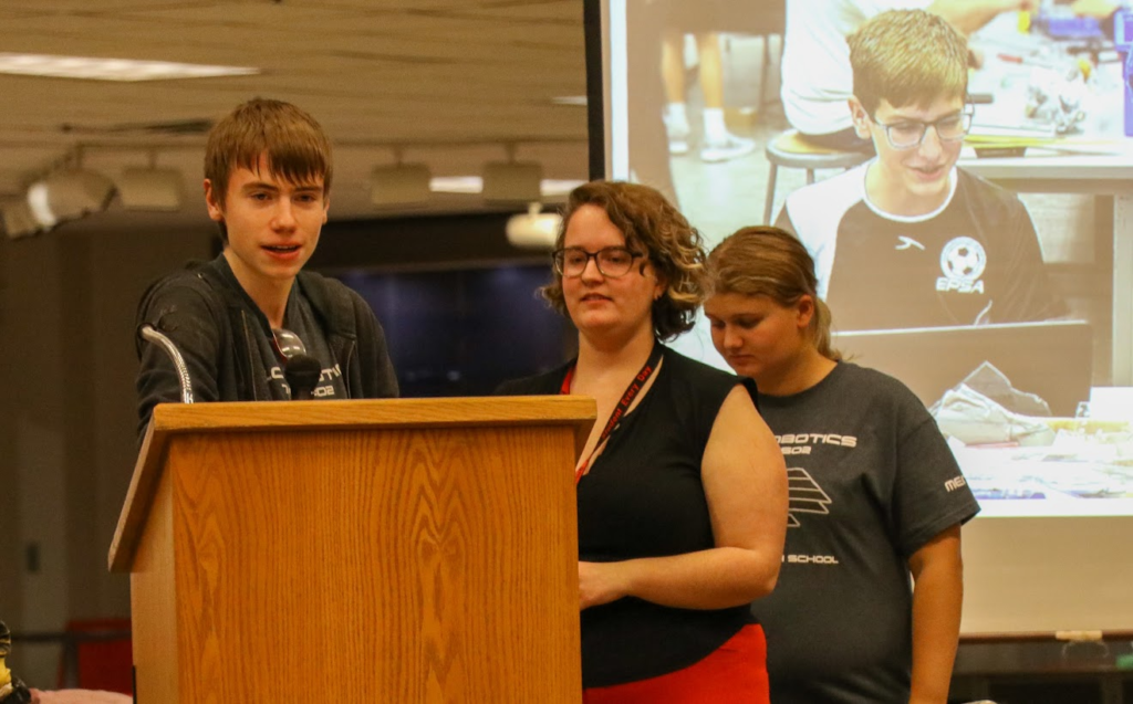 two mentors and one student talking on a podium 