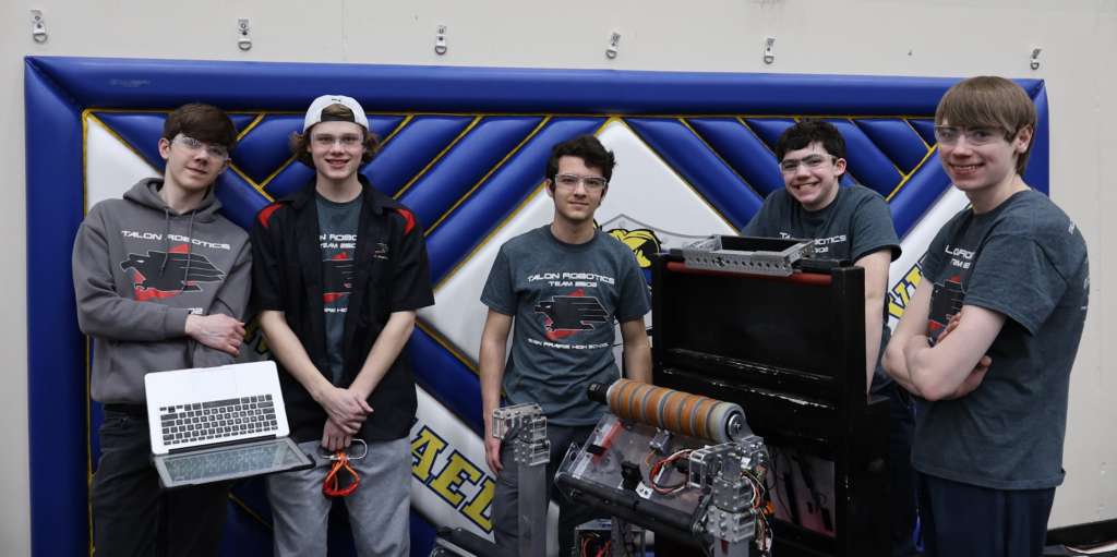 Five students smiling towards the camera with the robot