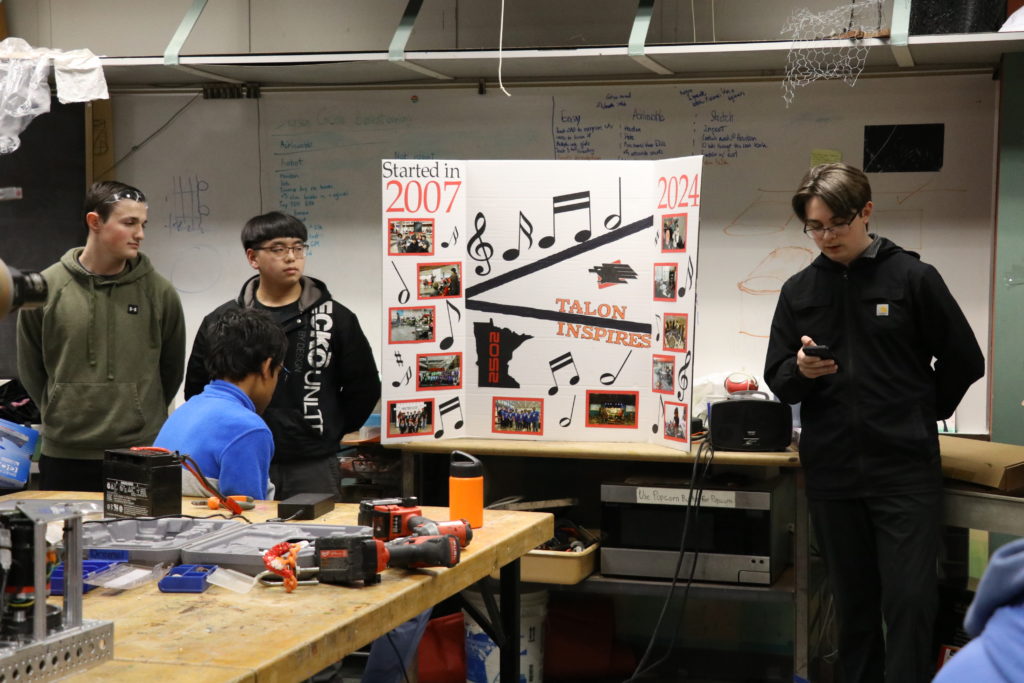 Three students giving a presentation with a decorated presentation board. 
