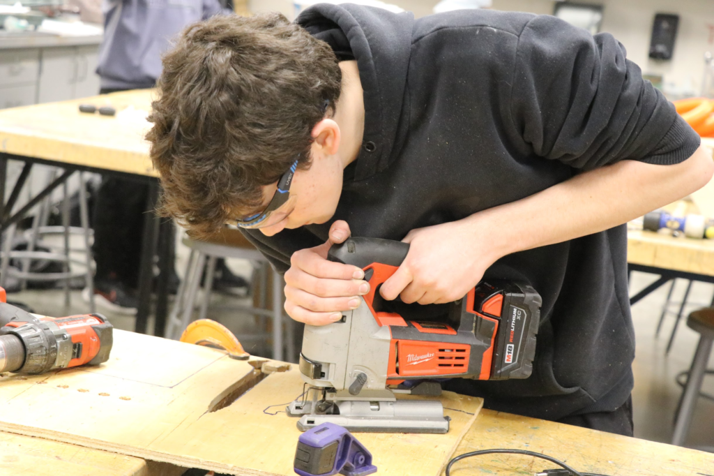 Robotics student using a jigsaw to cut parts out of wood.