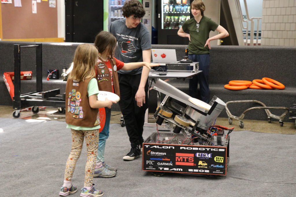 Two girl scouts feeding a disc into our older robot, Disco. 