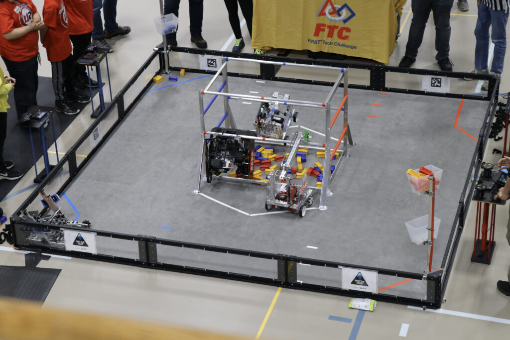 Four small bots on a field, climbing a structure and reaching for bars