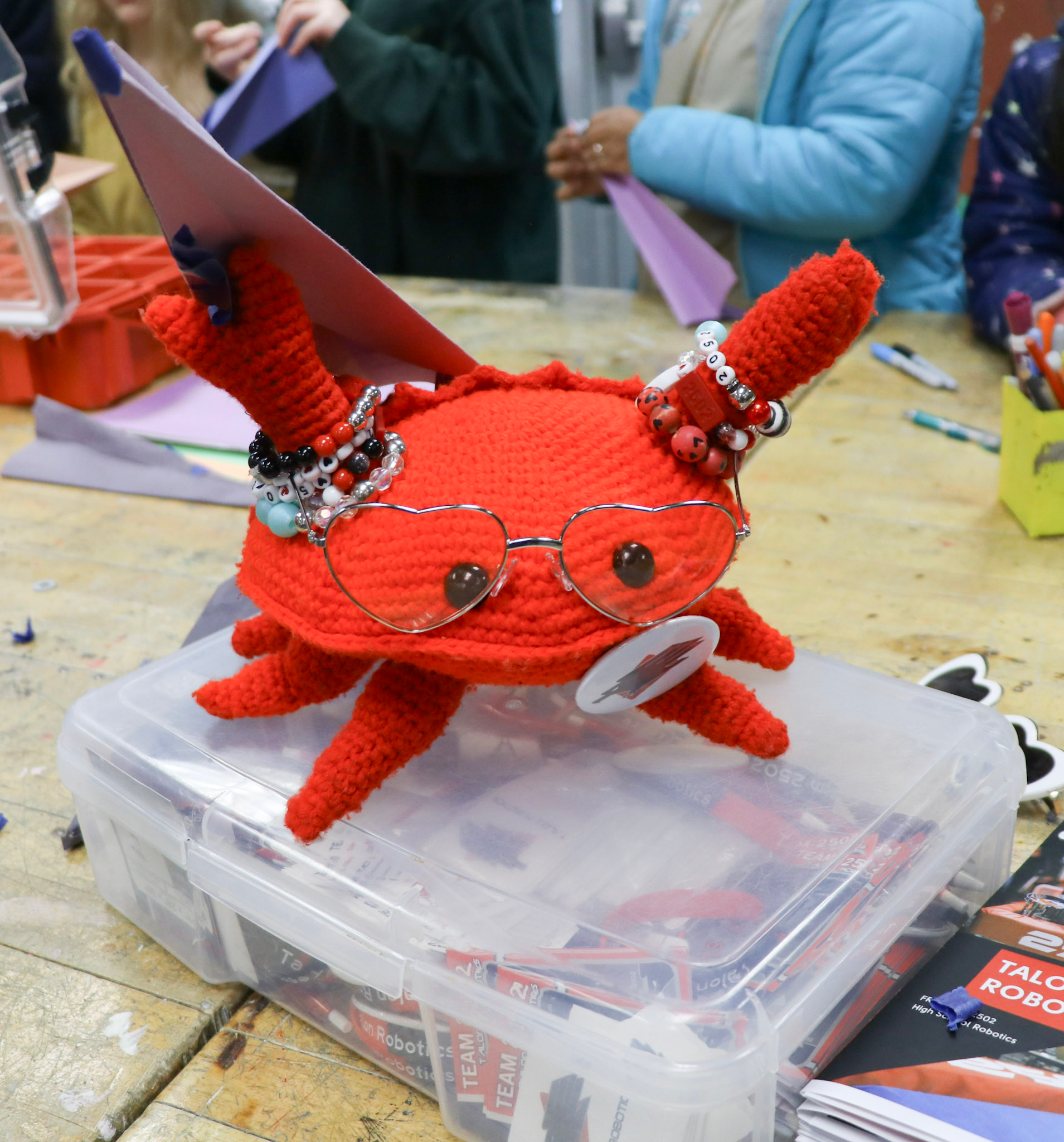 A crocheted crab based on the mascot of the programming language Rust holds a paper airplane. 