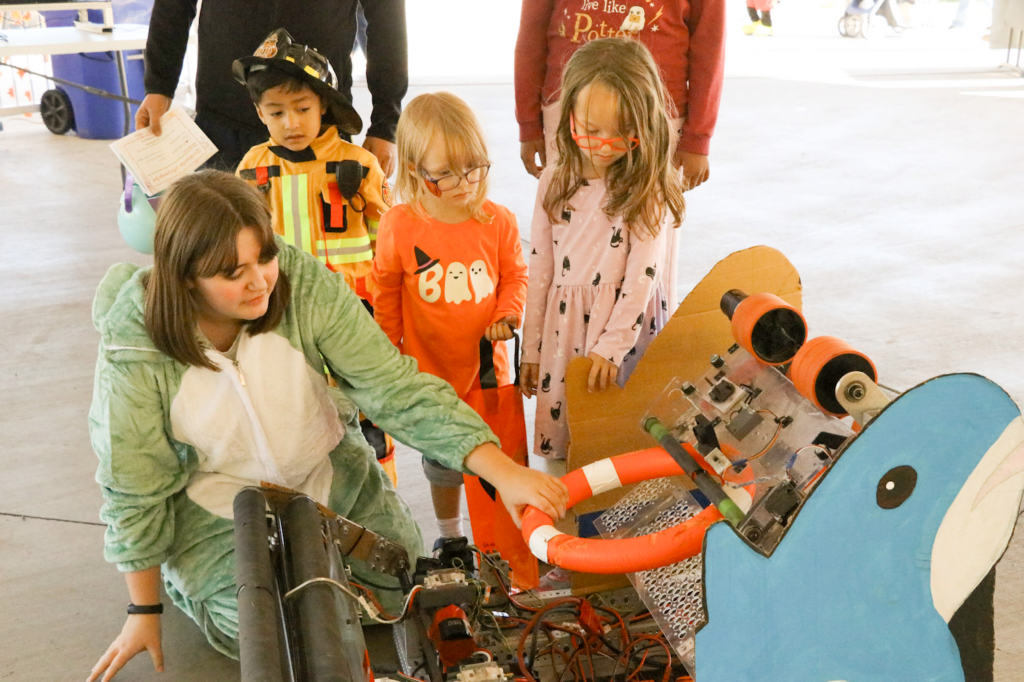 Charlotte on the ground showing kids how our robot works during an outreach event