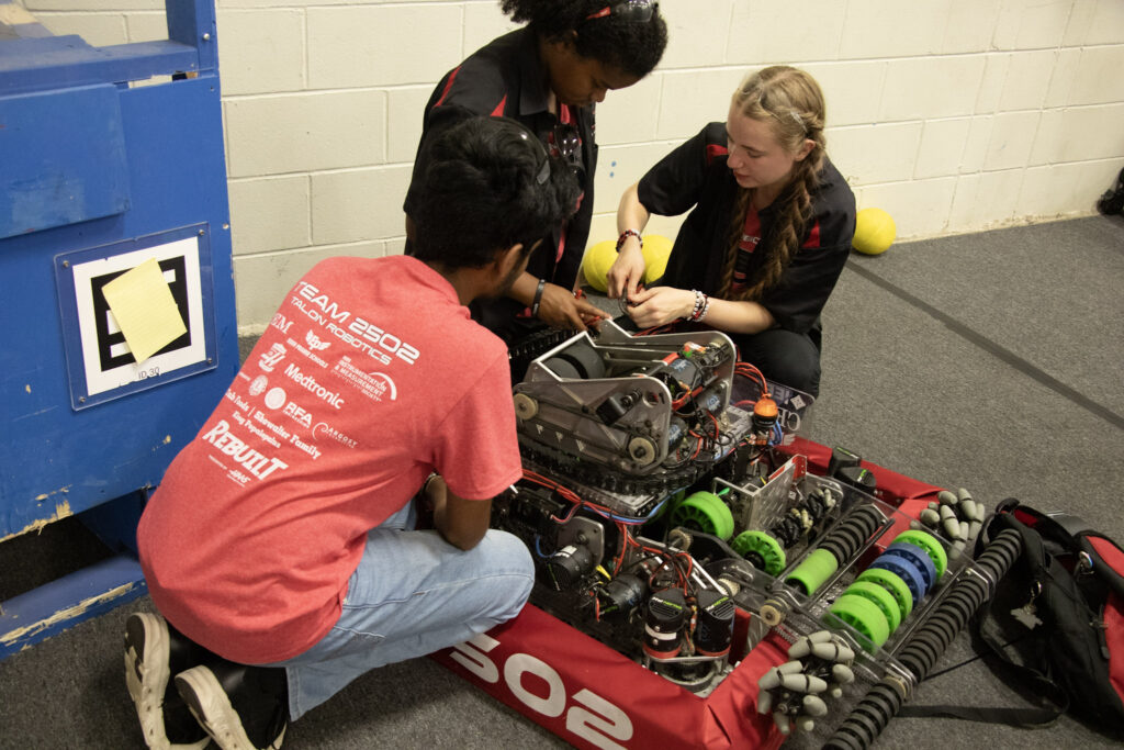 Image shows 3 talon build team members fixing our robot up at the fair
